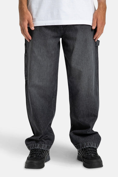 Jean denim gris clair large de DC SHOES, avec des poches à outils, associé à des sneakers noires et un T-shirt blanc.