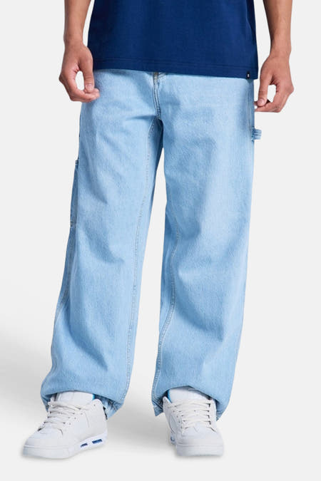 Lichtblauwe denim jeans van DC SHOES met een wijde pasvorm en timmermansdetails, gedragen met witte sneakers.