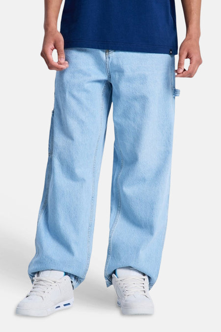 Lichtblauwe denim jeans van DC SHOES met een wijde pasvorm en timmermansdetails, gedragen met witte sneakers.