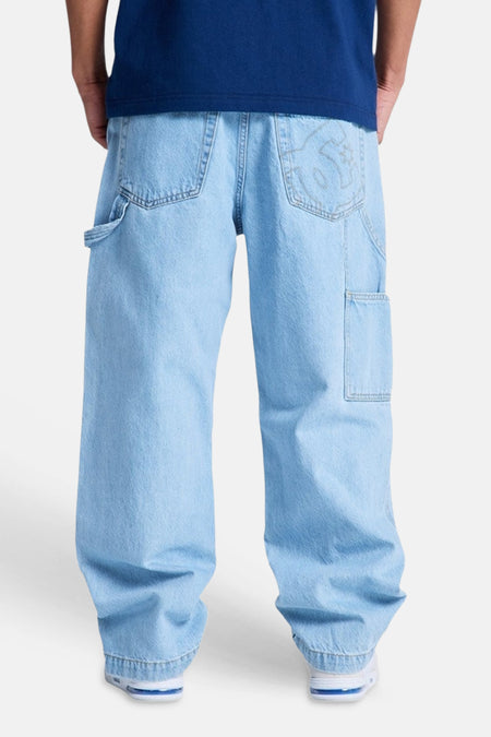 Lichtblauwe denim speciale pasvorm spijkerbroek van DC SHOES, achteraanzicht, met hamerlus en geborduurd logo, gedragen met donkerblauw T-shirt en witte sneakers.