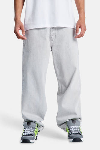Lichtgrijze denim jeans met speciale pasvorm van DC SHOES, gedragen door een persoon met een wit t-shirt en grijze sneakers met neon details.