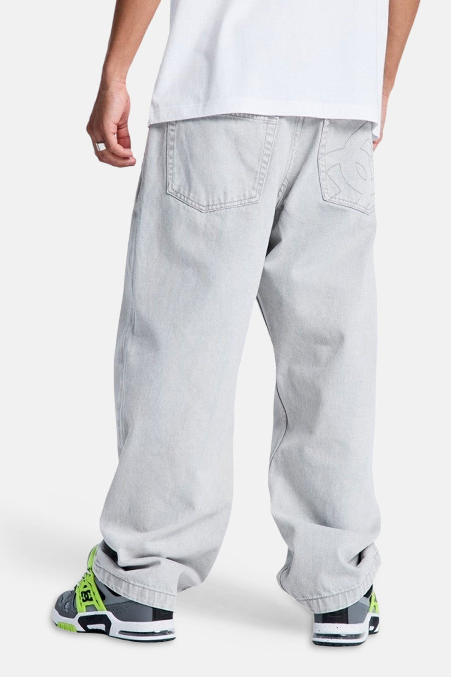 Lichtgrijze denim jeans met speciale pasvorm van DC SHOES, achterzijde met geborduurd DC-logo op de rechter achterzak, gedragen met wit T-shirt en grijsgroene sneakers.