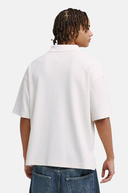 Witte oversized polo van DC SHOES met lichte textuur, achteraanzicht. Model met vlechten en jeans.