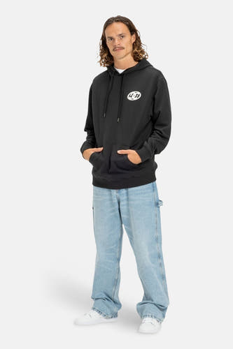 Zwarte sweater met kap van DC SHOES, met een logo op de borst, gecombineerd met wijde jeans en witte sneakers.