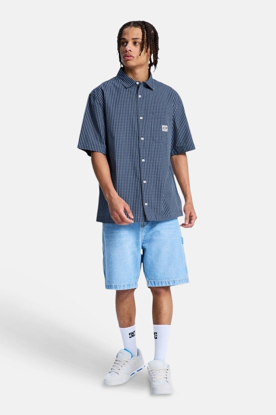 Chemise à carreaux bleus à manches courtes de DC SHOES, portée par un homme avec un short en jean et des baskets.