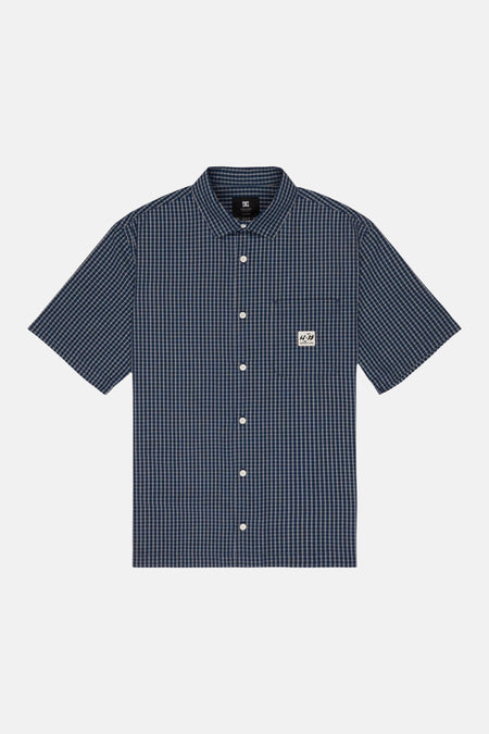 Chemise à carreaux bleus à manches courtes de DC SHOES, avec col pointu, boutons blancs et une poche poitrine.