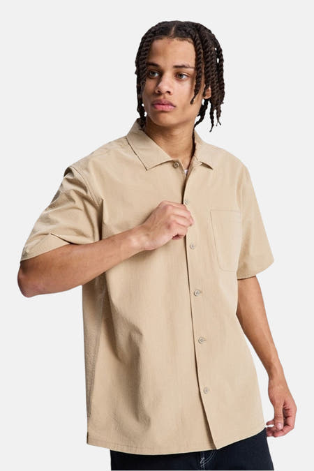 Chemise marron à manches courtes de DC SHOES, vue de dos, avec une texture lisse et portée avec un pantalon foncé.