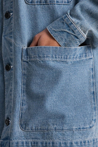 Veste en jean bleu clair de DC SHOES, avec une main dans la poche et des boutons sur le devant.