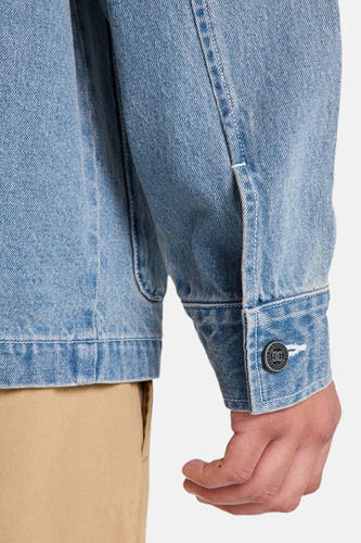 Veste en jean bleu clair de DC SHOES, avec un poignet boutonné et un pantalon kaki partiellement visible.