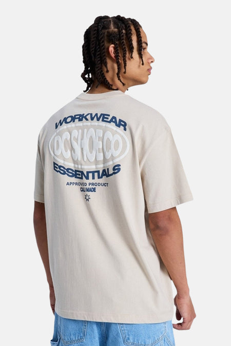 T-shirt beige à manches courtes de DC SHOES, dos avec grand imprimé : texte blanc en relief 'DC SHOE CO' dans un ovale et textes 'WORKWEAR' et 'ESSENTIALS' en bleu.