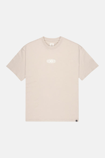 T-shirt beige à manches courtes de DC SHOES avec logo DC SHOE CO blanc sur la poitrine et petite étiquette DC sur l'ourlet.
