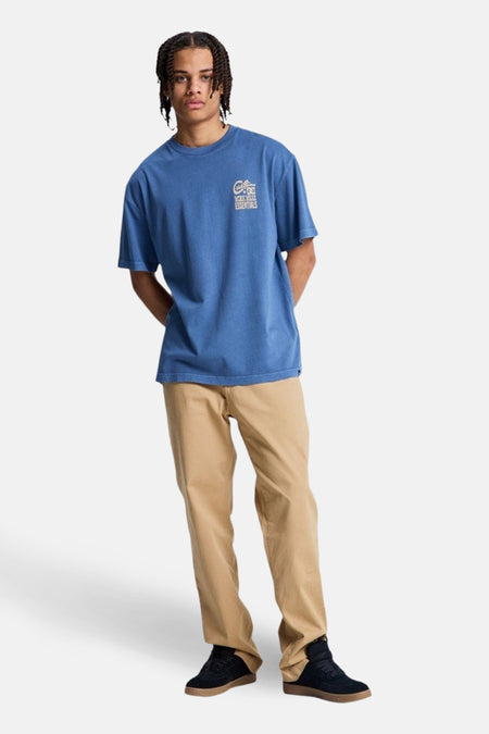 Blauw T-shirt met korte mouwen van DC SHOES, met een logo op de borst, gedragen met een kaki broek en zwarte schoenen.