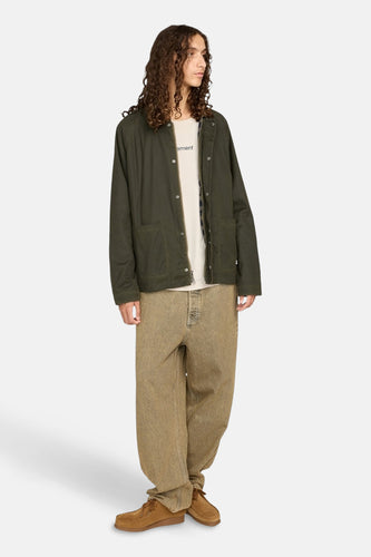 Man in groene jas, beige broek en bruine schoenen, staand.