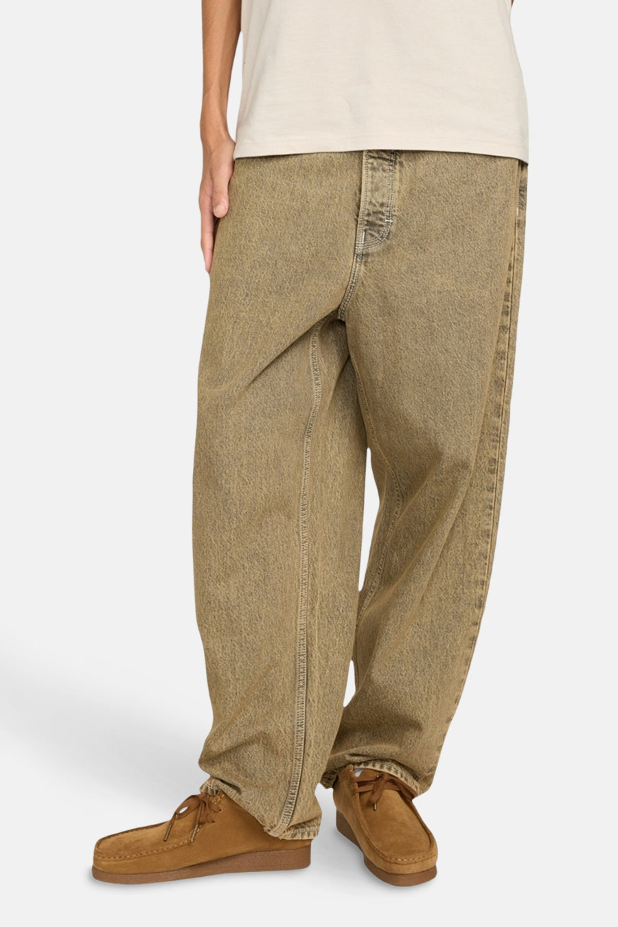 Een persoon draagt een beige T-shirt, bruine jeans en bruine suède schoenen.