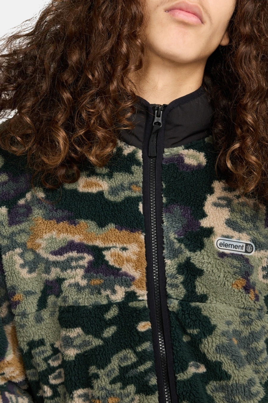 Close-up van iemand in een camouflage fleece jack met een zwarte rits en een "element" logo.