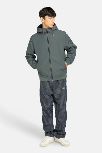 Manteau vert court d'ELEMENT, avec capuche et fermeture éclair noire, associé à un pantalon rayé et des chaussures blanches.