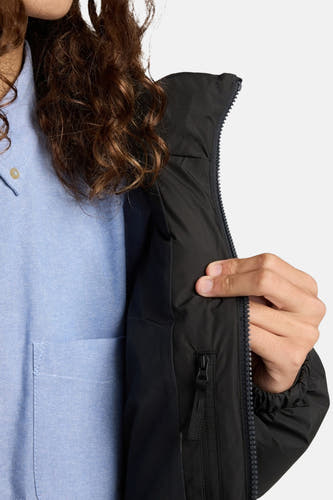 Manteau court noir d'ELEMENT, avec une fermeture éclair et une poche intérieure, porté sur un chemisier bleu clair.