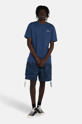 T-shirt bleu à manches courtes d'ELEMENT, avec un petit texte sur la poitrine. Porté avec des shorts camouflage et des baskets noires.