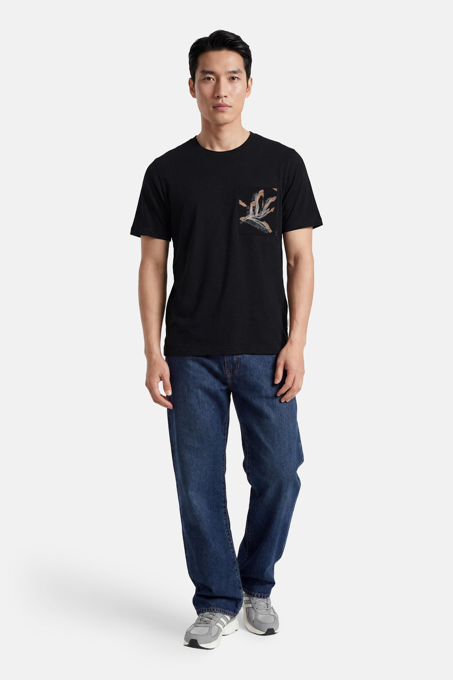 T-shirt noir ELEMENT avec une poche poitrine à imprimé abstrait dans des tons terreux, porté par un homme en jean bleu et baskets grises.