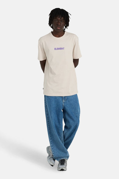 T-shirt beige à manches courtes de ELEMENT, avec nom de marque violet sur la poitrine, porté avec un jean ample et des baskets grises.