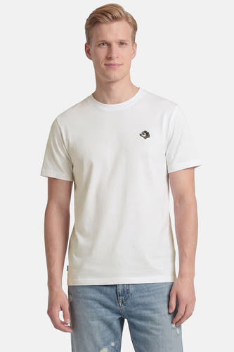 T-shirt blanc à manches courtes d'ELEMENT avec logo de dessin animé brodé sur la poitrine, porté par un homme en jean bleu clair déchiré.