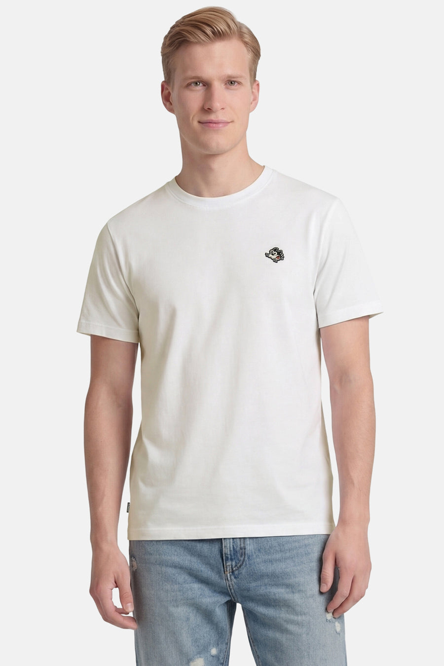 T-shirt blanc à manches courtes d'ELEMENT avec logo de dessin animé brodé sur la poitrine, porté par un homme en jean bleu clair déchiré.