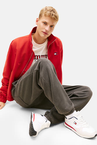 Des sneakers blancs de Tommy Jeans avec des accents rouges et bleu marine, portés avec un manteau rouge et un short de jogging gris.