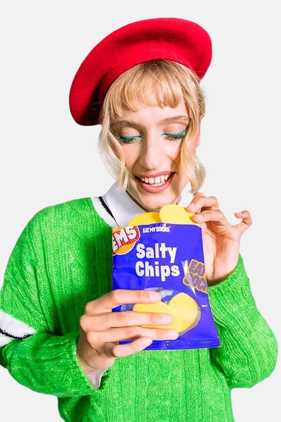 Blauwe sokken van EAT MY SOCKS in chipsverpakking, met gele chips en witte tekst, vastgehouden door model in groene trui en rode baret