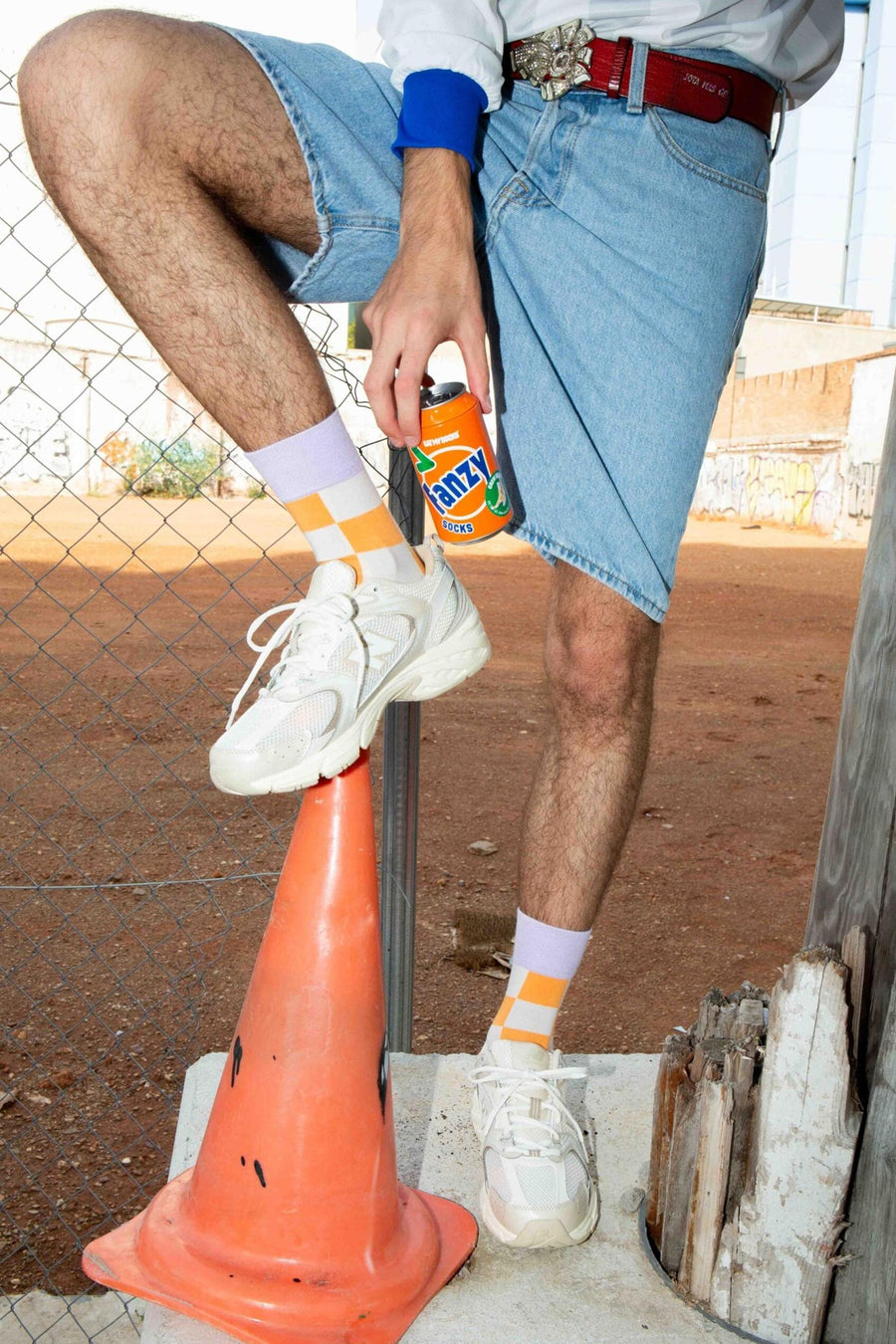 Oranje sokken met witte en lila ruitjes, van EAT MY SOCKS, gedragen met witte sneakers en denim shorts, lifestyle shot op oranje kegel
