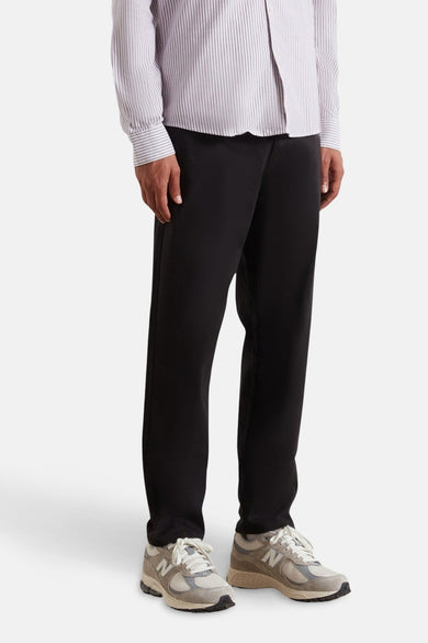 Pantalon noir de FARAH, avec une coupe décontractée et associé à un chemisier rayé et des baskets.
