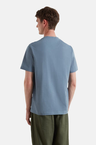 T-shirt bleu à manches courtes de FARAH, avec une impression sur le dos, associé à un pantalon vert.