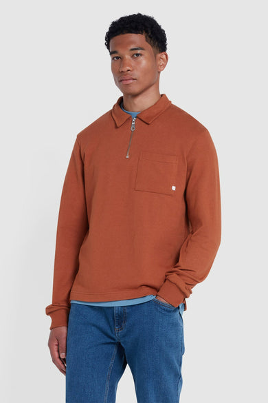 Oranje sweater van FARAH, met lange mouwen, een kraag en een ritssluiting, gedragen over een blauw shirt en jeans.
