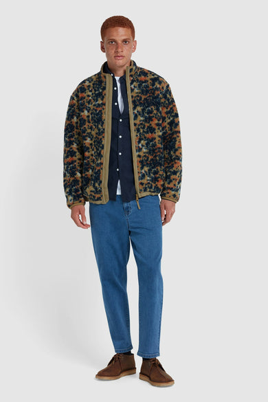 Fleece multicolore de FARAH, avec un motif floral frappant, porté sur une chemise et des jeans bleus avec des chaussures marron.