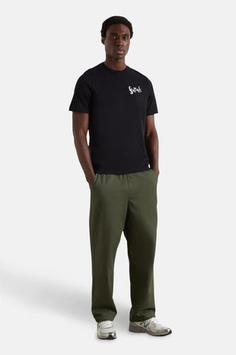 T-shirt noir à manches courtes de FARAH, avec une impression de texte blanche sur la poitrine, associé à un pantalon vert et des baskets grises.