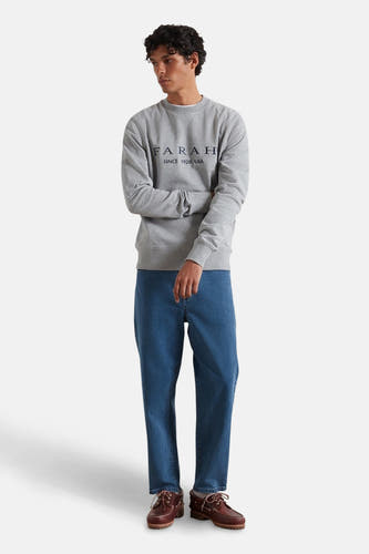 Pull gris de FARAH, avec des manches longues, associé à des jeans et des bottes brunes.