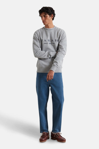 Pull gris de FARAH, avec des manches longues, associé à des jeans et des bottes brunes.