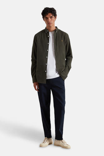 Chemise verte à manches longues de FARAH, portée sur un T-shirt blanc avec des pantalons bleu marine et des baskets crème.