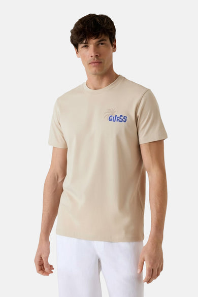 T-shirt beige à manches courtes de Guess, avec logo bleu et imprimé palmier.