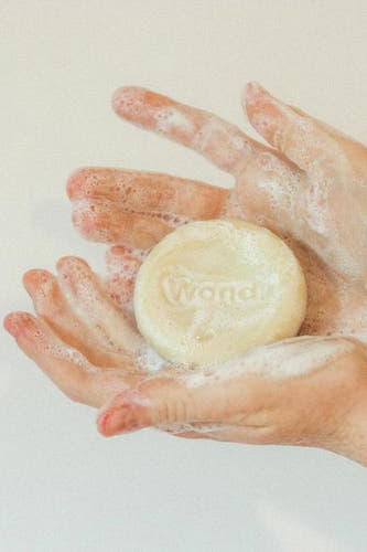 Ligne de soin ronde et blanche comme du beurre de WONDR CARE, tenue dans des mains mousseuses.