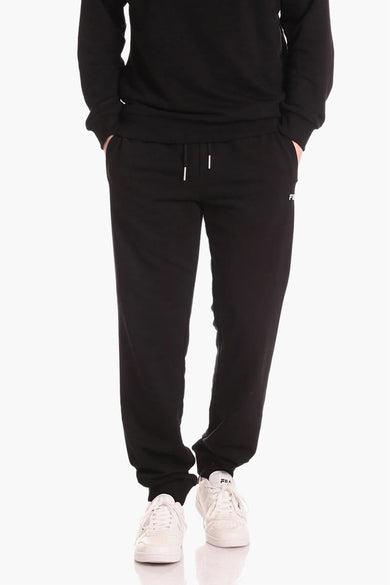 Pantalon de jogging noir FILA avec cordons blancs et petit logo sur la jambe, porté avec un sweat à capuche noir et des baskets blanches, vue de face.