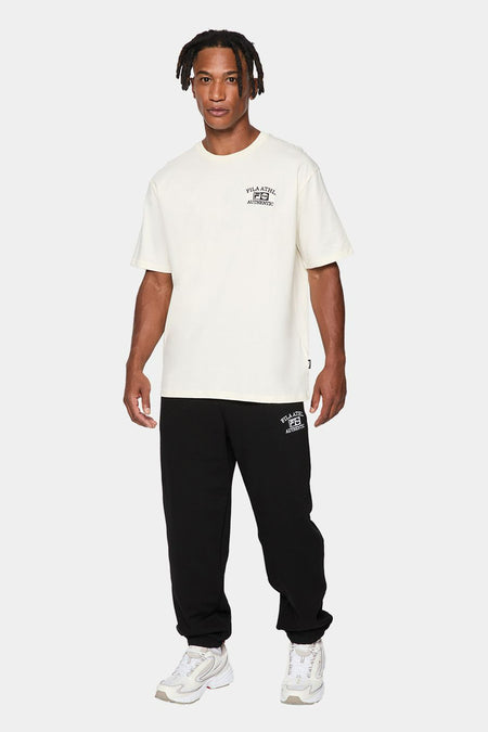 Ecru T-shirt met korte mouwen van FILA, met logo op de borst, gecombineerd met zwarte joggingbroek en witte sneakers.
