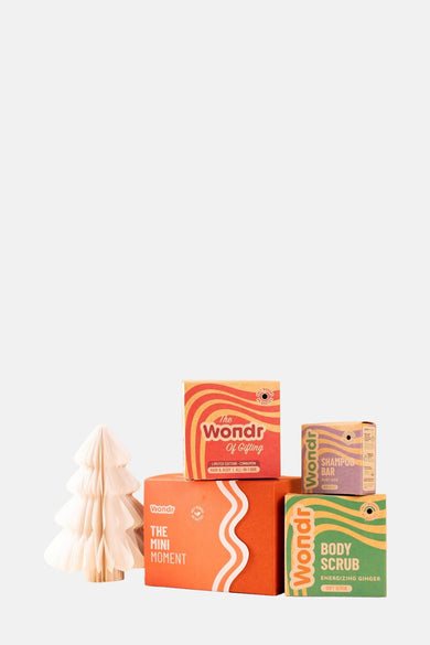Articles de cadeau multicolores de WONDR CARE, empilés avec un arbre de Noël décoratif en papier sur le côté.