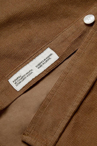 Chemise brune à longues manches de POMPEII, étiquette avec des détails de marque visibles, texture corduroy et fermeture à boutons.