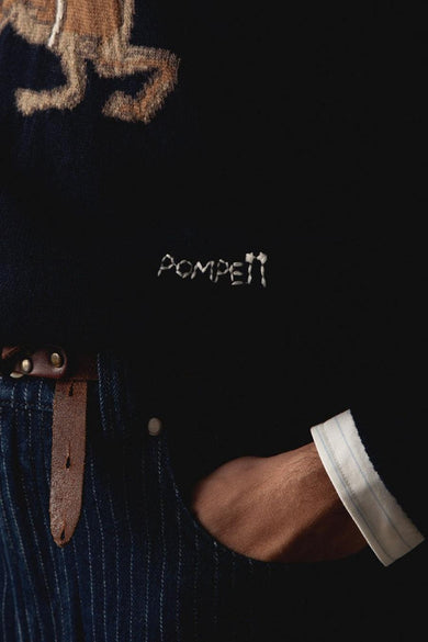 T-shirt bleu avec col rond de POMPEII, doté de détails brodés et d'une ceinture en cuir marron sur un pantalon rayé.