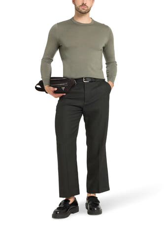 Zwarte schoudertas van Guess, met zilverkleurige details, gedragen op de heup met een grijze trui en donkere pantalon.