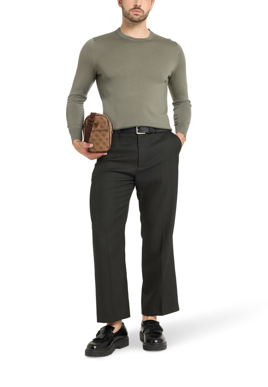 Man in grijze trui, zwarte broek en leren loafers met een GUESS-tas.