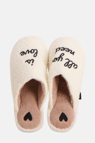 Twee crèmekleurige pantoffels met borduurwerk en een hart.