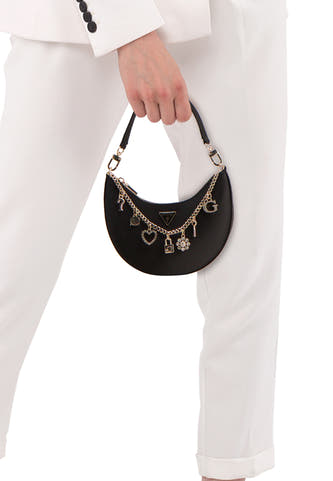 Sac à bandoulière noir Guess® avec chaîne dorée et différents charms, porté par une personne en costume blanc.