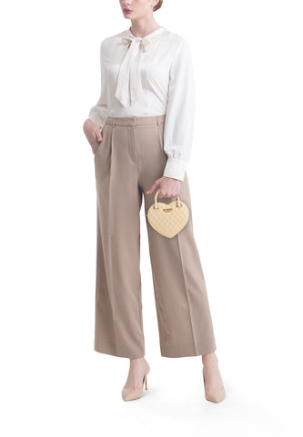 Sac à dos Guess de couleur jaune, en forme de cœur et avec un motif carreaux, porté avec une blouse blanche et un pantalon beige.