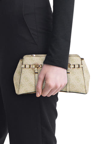 Sac à bandoulière beige Guess® avec un imprimé logo intégral et un détail de boucle dorée, porté par une personne en tenue noire.